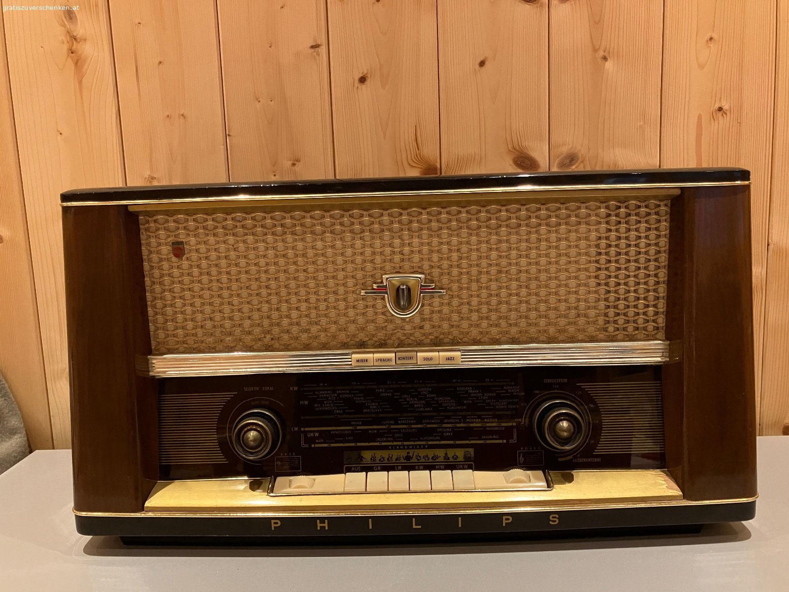 Alter Philips Röhrenradio / Vintage-Radio – funktionstüchtig. Verschenke einen alten Philips Radio im klassischen Holzgehäuse aus früheren Jahrzehnten.

Das Gerät ist funktionstüchtig und auch optisch für sein Alter noch in einem schönen Zustand. Ein dekoratives Stück für Liebhaber alter Radios, Sammler oder auch als Vintage-Dekoration.

Der Radio verfügt über die klassischen Wellenbereiche LW, KW, MW und UKW sowie verschiedene Klangtasten.

Der Lautstärkeregler sollte einmal gereinigt bzw. gewartet werden, ansonsten funktioniert das Gerät. Aufgrund des Alters wird es natürlich ohne Garantie auf dauerhafte Funktion abgegeben.

Abmessungen ca.:

* Breite: 60 cm
* Höhe: 38 cm
* Tiefe: 24 cm

Das schöne Holzgehäuse, die große Senderskala und die typische Stoffbespannung machen den Philips auch optisch zu einem schönen Zeitzeugen.

Gratis gegen Selbstabholung.
Vielleicht findet sich ein Liebhaber, der Freude daran hat und den Radio weiter verwendet oder restauriert.

Privatabgabe, keine Garantie oder Gewährleistung.